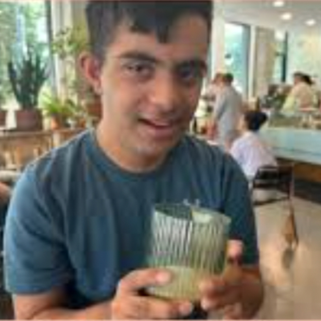 A photo of Sid, a South Asian man who is wearing a blue t shirt and holding a glass.